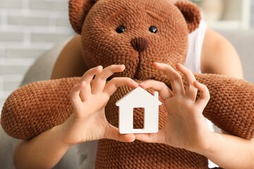 Girl with house figure and toy bear at home, closeup. Adoption concept