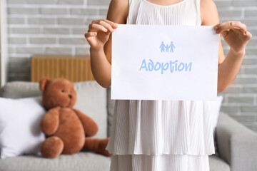 Girl holding paper with word ADOPTION at home, closeup