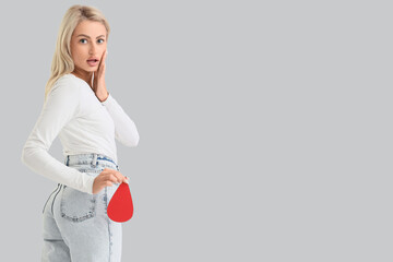 Shocked young woman with paper blood drop on light background. Menstruation concept