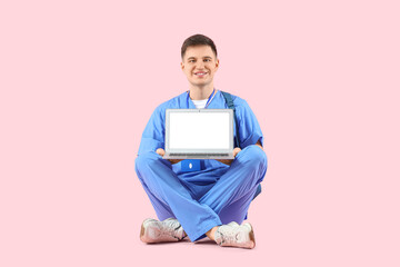 Male medical intern with blank laptop sitting on pink background