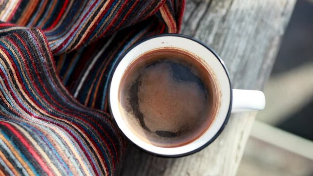 coffee in a white kitchen cup on a wooden bench in the park, a walk in the forest, a scarf and coffee, a winter hike in the forest, a rest in a winter park, a striped bright scarf and hot tea