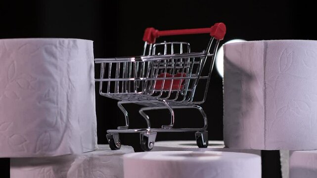 Hand placing toilet paper roll near shopping cart on black background