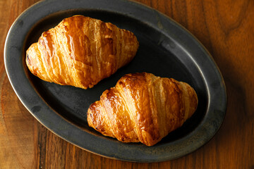 黒い皿に乗せた焼き立てクロワッサン　木製テーブルの背景