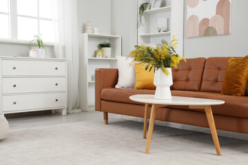 Vase with mimosa flowers on table in light living room interior