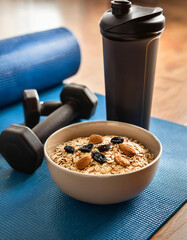 Bowl of Oats with Almonds and Dried Fruits, Protein Shaker, and Dumbbells on a Blue Yoga Mat