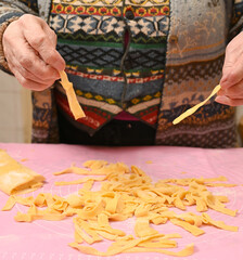 Woman skillfully shaping and cutting fresh pasta in a warm kitchen environment