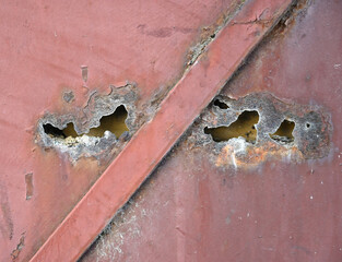 Rusty metal surface revealing holes and corrosion patterns created by weathering over time in an...