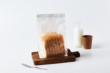 Sliced Bread in Clear Packaging on a Wooden Board With a Glass of Milk and a Wooden Cup
