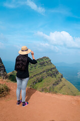 A female traveler  wearing a hat and posing by looking towards the view of Deviramma Betta in Chikkamagaluru, Karnataka, India