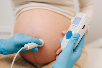 Gynecologist listens to fetus heartbeat with fetal doppler in the clinic. Gynecologist checks heart...