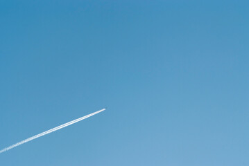 airplane in flight and white stripe against blue sky