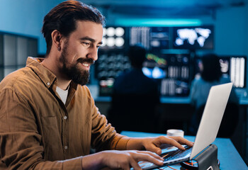 Stock trader analyzing financial data on laptop, working late in monitoring room with multiple screens displaying real-time charts and graphs. Financial investment and technology concept