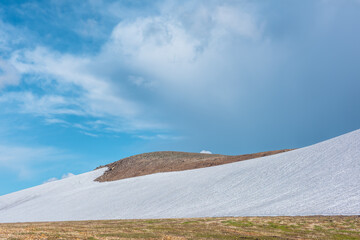 Scenic view to glacier on stone hillside under clouds in blue sky. Rock hill with snow on high...