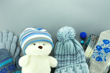 A toy bear in a hat, mittens, gloves on a gray background. There is space for text. A funny photo with a bear in clothes.