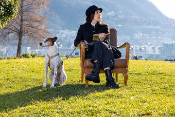 Portrait of a beautiful girl sitting in an armchair in a public park with a very obedient dog next...