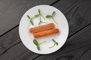 Two cooked sausages on a white plate with sunflower sprouts arranged around.