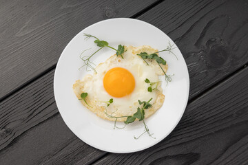 A fried egg with vibrant yellow yolk and green sprouts on a white plate.