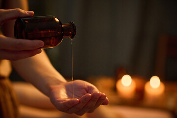 Medium close up of unrecognizable female hand holding jar and pouring essential oil into palm