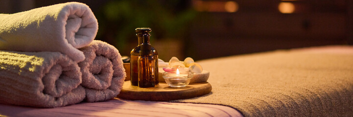Website banner of three towel rolls, oval tray with jar filled with essential oil and lit tea candle