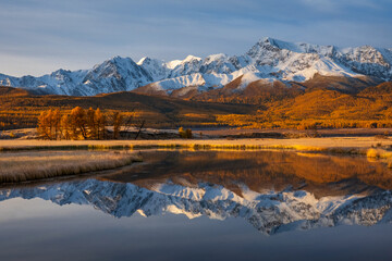 Obraz premium Serene autumn landscape showcasing a calm water reflection of snowy mountains and vibrant foliage.