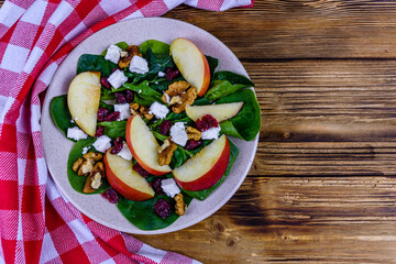 Salad with spinach leaves, feta cheese, cranberries, walnuts and apple in a ceramic plate. Top view