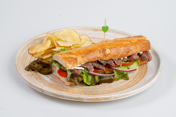 delicious sandwich with sliced beef, fresh vegetables, and side of chips, garnished with toothpick. Perfect for satisfying meal