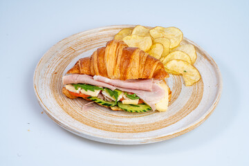 Delicious croissant sandwich with ham, cheese, and fresh vegetables served with potato chips. Perfect for light lunch or snack