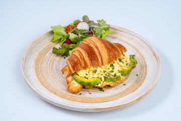 Delicious croissant sandwich filled with scrambled eggs and avocado, served with fresh salad. Perfect for breakfast or brunch