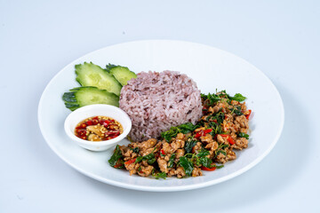 Delicious plate of stir fried meat with basil, served with purple rice, cucumber slices, and dipping sauce, showcasing vibrant colors and flavors