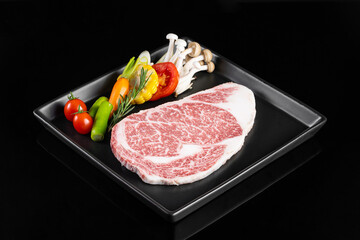 Fresh marbled beef steak with colorful vegetables on black plate, showcasing vibrant arrangement of tomatoes, peppers, and mushrooms, perfect for gourmet meal