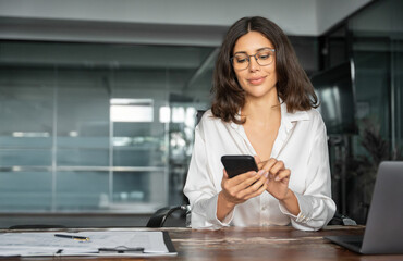 Middle aged Hispanic business manager ceo using cell phone mobile app, laptop. Smiling Latin or...