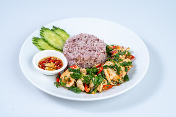 Delicious plate of stir fried chicken with basil, served with purple rice, cucumber slices, and dipping sauce, showcasing vibrant colors and fresh ingredients