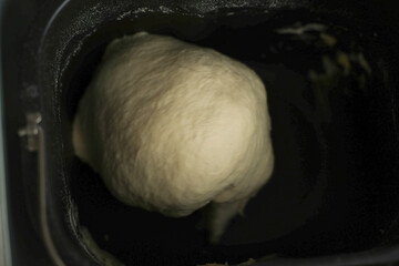 The concept of dough preparation, dough kneading, kitchen appliances for kneading text. A close-up view of the dough in a black bowl from above, flour is visible on the sides. High quality photo