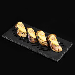 Grilled fish with apple slices served on black slate plate, showcasing modern culinary presentation. dish combines savory and sweet flavors, creating appealing visual