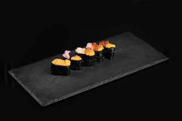 Sushi rolls arranged on black slate plate, showcasing various toppings and colors, creating appetizing presentation