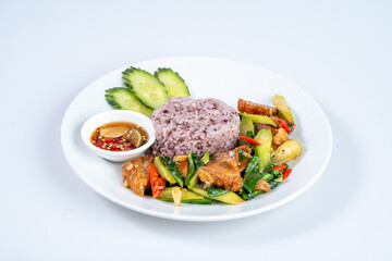 Delicious plate of purple rice with stir fried vegetables, crispy pork, and cucumber slices, served with side of dipping sauce for flavorful meal