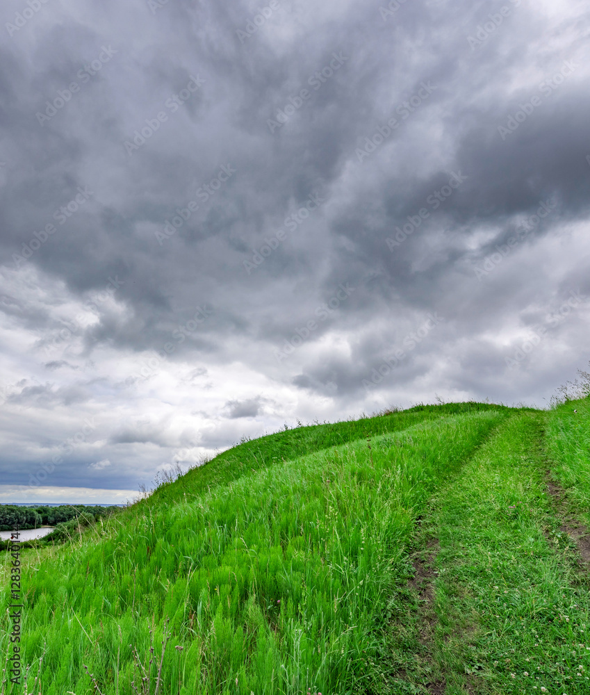 Wall mural Hill covered in green grass and a cloudy sky