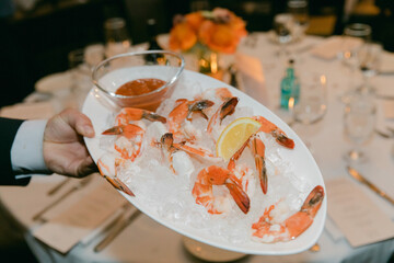 Shrimp cocktail served on a platter at an elegant dining event with lemon and sauce