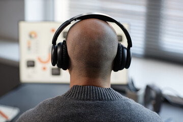 Rear view of bald man listening to music wearing headphones to focus on work while using computer...