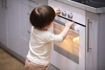 Little boy playing with oven in kitchen. Dangerous situation