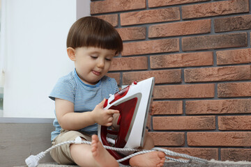 Little boy playing with iron at home. Child in danger