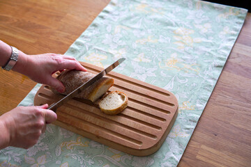 High angle view of wooden breadboard lying on oak table with women hands cutting bread with place...