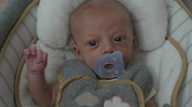 Cute Little Infant Boy Sucking on Pacifier in his Baby Seat