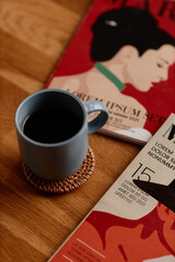 Vertical shot of ceramic cup with black coffee placed on handmade woven coaster made of straw protecting surface of wooden table in cozy living room, copy space