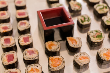 Colorful sushi rolls arranged neatly with a dipping sauce carved in a square container on a white surface