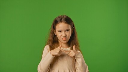 Little girl child makes grimaces funny faces, poses and sticks out tongue, positive expression, isolated on chroma key green screen studio background mockup.