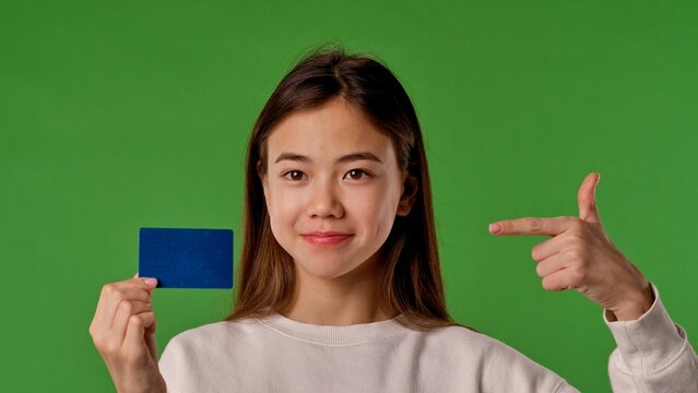 Asian girl child holding advertisement card and pointing finger at blue space, positive expression, isolated on chroma key green screen background mockup.