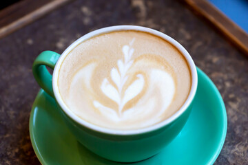 Fresh tasty aromatic coffee latte with foam and pattern in green cup on table. Delicious breakfast. Selective focus