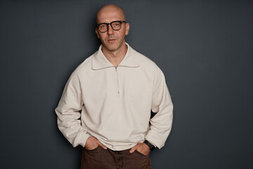 Medium full shot of confident middle aged man with shaved head wearing white half zip sweatshirt showcasing fashionable outfit captured against grey wall in studio, copy space © Seventyfour