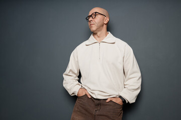 Medium full shot of middle aged man with buzzcut wearing white half zip sweatshirt posing with hands in pockets against grey wall in studio, copy space © Seventyfour